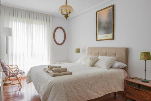 a white bedroom with a large bed and a mirror at Casa marinera con piscina y jardín. in Colindres