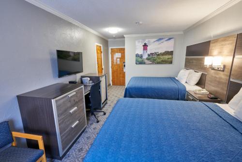 a hotel room with two beds and a desk and a television at Ambassador Inn and Suites in South Yarmouth