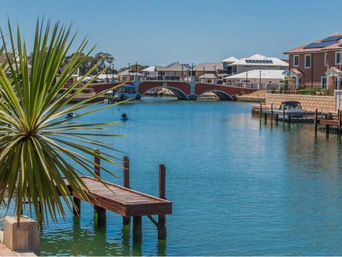 a bench sitting next to a river with a bridge at "WATERLILY HOUSE" - Luxury Canal House, Jetty, Dog & Child Friendly - Sleeps 14 in Mandurah