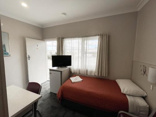 um pequeno quarto com uma cama e uma televisão em Hillview Motel em Goulburn