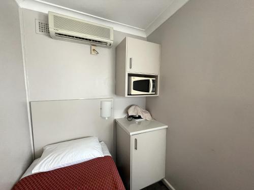 a small white room with a microwave and a bed at Hillview Motel in Goulburn