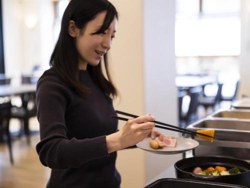 a woman holding a plate of food with chopsticks at Ariston Hotel Kyoto Jujo in Kyoto