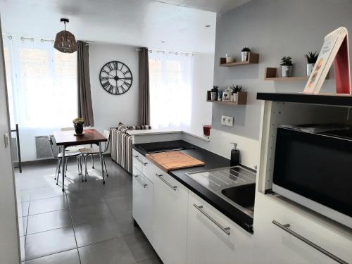 Il comprend une cuisine équipée d'une cuisinière, d'une table et d'une horloge. dans l'établissement Appartement centre ville rue calme 2 pièces classé 3 étoiles, à Lannion