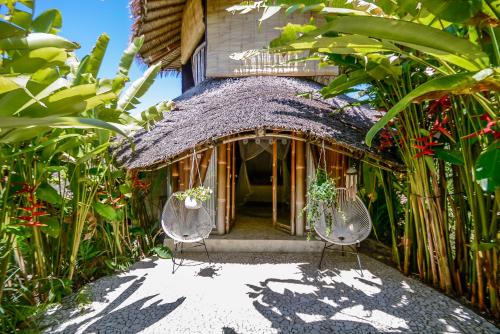 a house with a thatched roof with two chairs at Le Bamboo Bali in Uluwatu