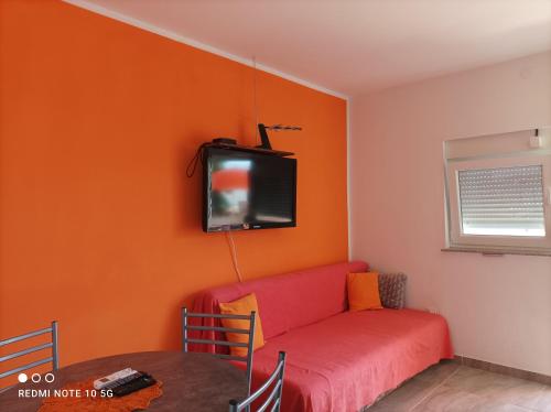 a living room with a red couch and a tv on the wall at Apartmani Pablo in Pag