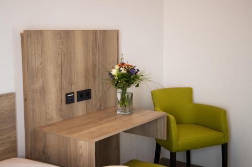 a vase of flowers on a table next to a green chair at Albhotel Bahnhöfle in Stubersheim