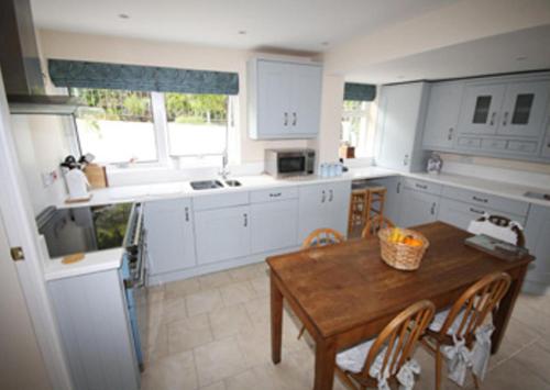 a kitchen with white cabinets and a wooden table at Spacious Detached House with Parking & Views in Fowey