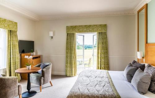 a room with a bed, chair, tv and window at Buxted Park Country House in Buxted