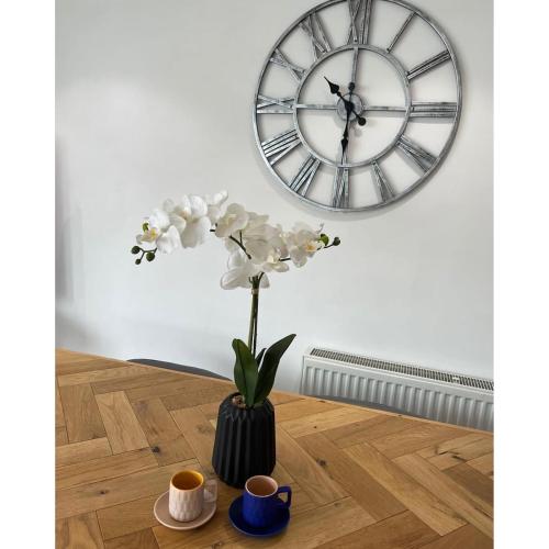 a vase with flowers on a table in front of a clock at The Hideout (Garden Flat, 4 Dragon Road) in Harrogate