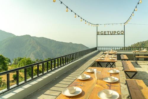 a row of tables on a balcony with mountains in the background at The Hosteller Kareri in Dharamshala