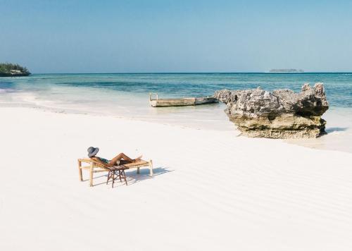 - une table et une chaise sur une plage de sable blanc dans l'établissement Sunshine Bay Hotel Zanzibar, à Matemwe