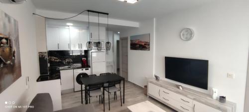 ein Wohnzimmer mit einem TV, einem Tisch und Stühlen in der Unterkunft Apartamentos Sol y Luna Conil in Conil de la Frontera