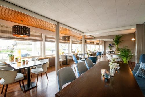 ein Restaurant mit Tischen, Stühlen und Fenstern in der Unterkunft Strandhotel de Vassy in Egmond aan Zee