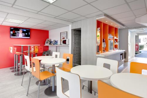 a restaurant with white tables and orange chairs at Première Classe La Roche Sur Yon - Vendéspace in Mouilleron-le-Captif