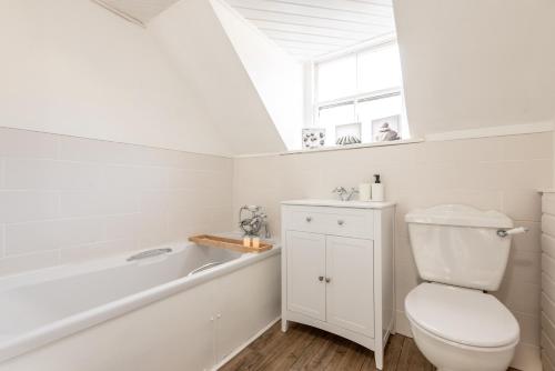 a white bathroom with a toilet and a bath tub at Charming Cardoon Cottage in beautiful village in Comrie