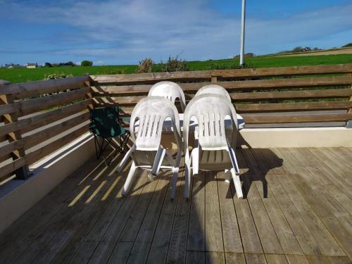 3 sillas blancas sentadas en una terraza de madera en Ty cocooning, en Kerlouan