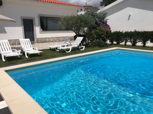 a swimming pool with two chairs and a house at Ribeirinho da Serra in Penela
