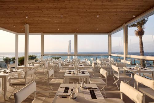 a restaurant with white tables and chairs and a view of the ocean at Dimitra Beach Hotel & Suites in Agios Fokas