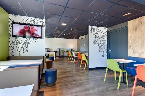 a dining room with tables and chairs and a tv on the wall at ibis budget La Roche Sur Yon Vendespace in Mouilleron-le-Captif