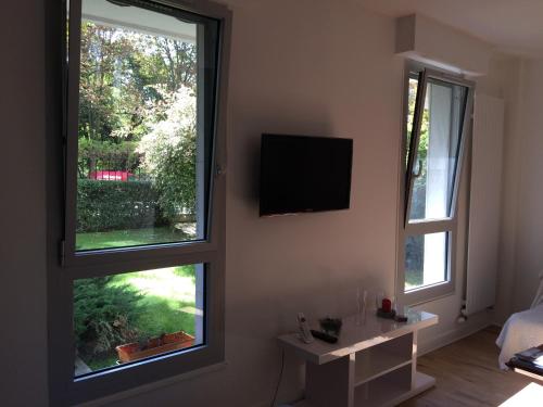 a living room with two windows and a television at Trés Beau Studio (face bois), 10mn de l'Etoile in Neuilly-sur-Seine