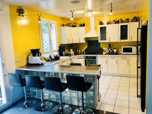 a kitchen with yellow walls and a counter with bar stools at Villa de 4 chambres avec piscine privee sauna et jardin clos a Villemeux sur Eure in Villemeux-sur-Eure