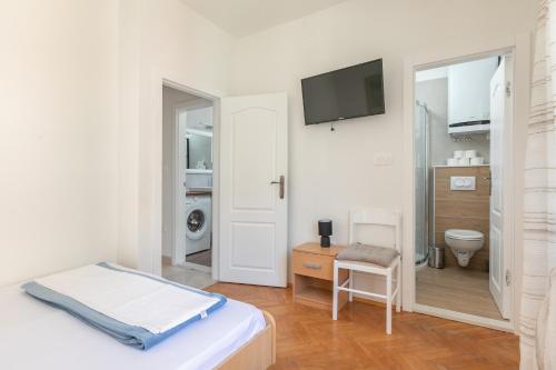 a white bedroom with a toilet and a tv on the wall at Apartman Ana Borić in Podgora