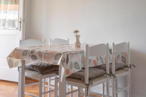 a dining room table with white chairs and a vase on it at Apartman Ana Borić in Podgora