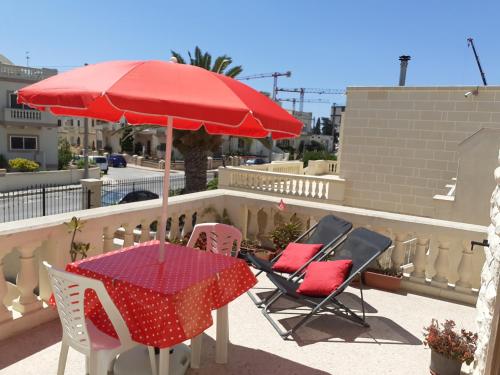 a table and chairs and a red umbrella on a balcony at Sunny large terrace studio apartment WiFi Airconditioners BBQ in Mellieħa