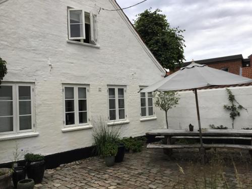 ein weißes Haus mit einem Tisch und einem Regenschirm in der Unterkunft Rebslagerhuset in Ribe