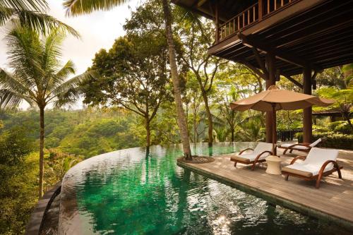 a pool at a resort with chairs and an umbrella at COMO Shambhala Estate - CHSE Certified in Payangan