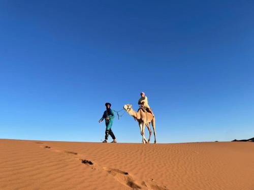 two men riding a camel in the desert at Aladdin Desert Lodge - Mhamid Sahara Camp in El Gouera