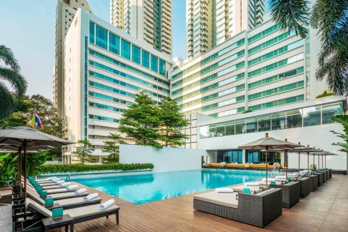 曼谷的住宿－COMO曼谷大都會酒店，一张酒店游泳池的图片,里面摆放着椅子和遮阳伞
