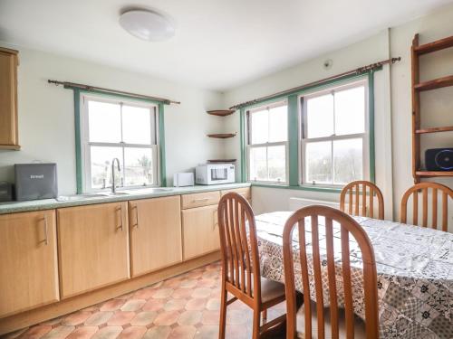 a kitchen with a table and chairs and two windows at Shaw Cottage in Dumfries