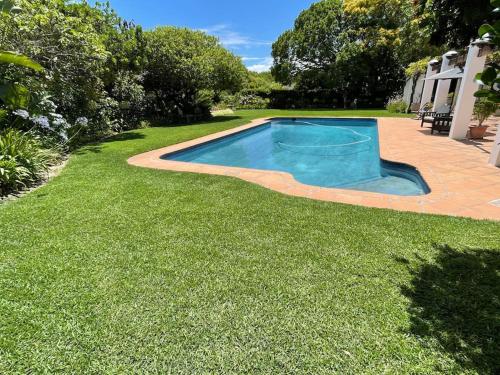 una piscina en un patio con césped verde en Charming Guest Suite in the Constantia Wine Valley en Ciudad del Cabo