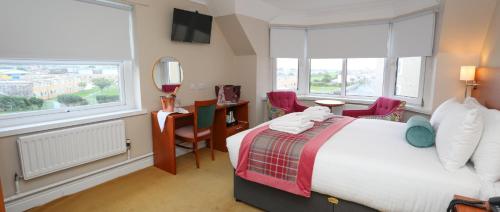 a bedroom with a bed and a desk and windows at The Beaches Hotel and Spa in Prestatyn