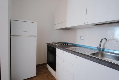 a white kitchen with a sink and a refrigerator at Nuraghe Apartments in Teulada