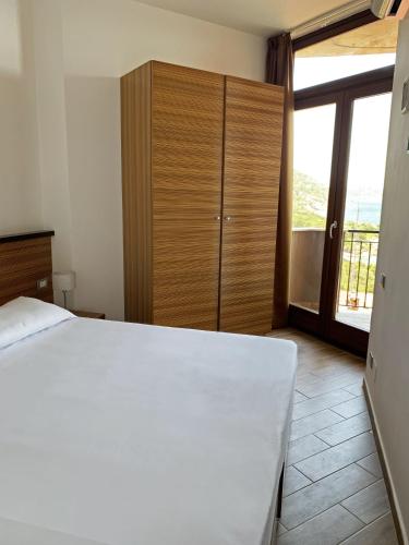 a bedroom with a white bed and a wooden cabinet at Nuraghe Apartments in Teulada