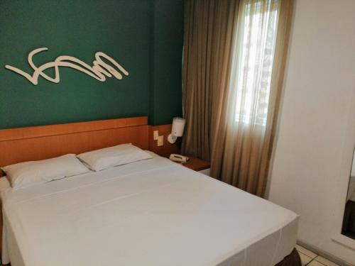 a bedroom with a white bed and a green wall at Condomínio Bristol Praia do Canto Apart Hotel in Vitória