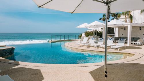 a swimming pool with chairs and umbrellas next to the ocean at Beachfront Flats Los Cabos in San José del Cabo