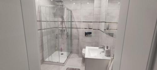 a white bathroom with a shower and a sink at Apartamenty Przystań in Ełk