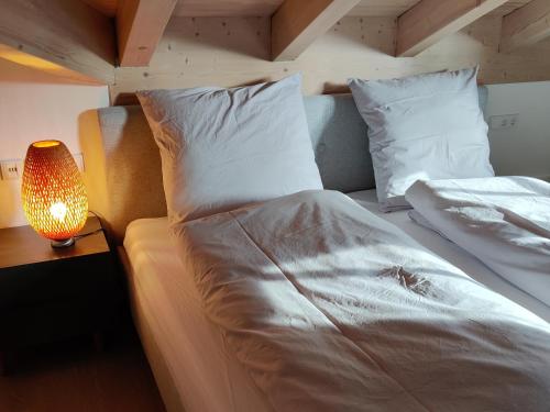una cama con sábanas blancas y una lámpara sobre una mesa en Chesa Piz en Pfronten