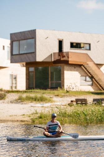 a man in a kayak on the water in front of a house at Jaukūs ART stiliaus apartamentai antrame aukšte su vaizdu į marias in Svenele