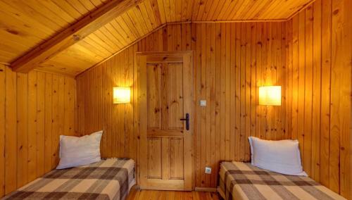two beds in a room with wooden walls and two lights at Hotel FAMIL - adults only in Bansko