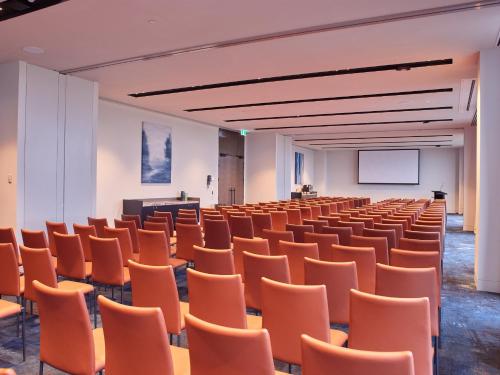 an empty lecture hall with orange chairs and a podium at Hyatt Place Melbourne Caribbean Park in Scoresby