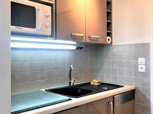une cuisine avec un évier et un micro-ondes dans l'établissement Appartement rénové au pied des pistes avec 2 balcons, piscine et WiFi - FR-1-267-198, au Corbier
