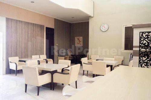 Un comedor con sillas y mesas blancas y un reloj. en My Hommy Homestay Mitra RedDoorz, en Surabaya