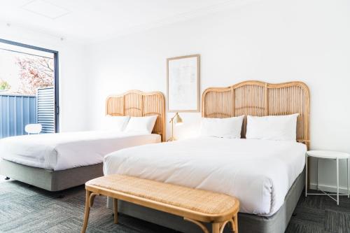 two beds in a hotel room with a bench at The Ned Ryan Motel in Boorowa