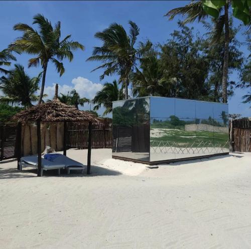 a bench on the beach with a fence and palm trees at Mirror House Watamu in Watamu