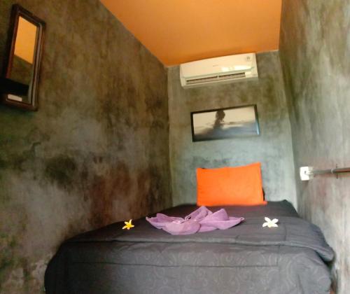 a small bedroom with a bed with an orange pillow at Keramas Surf Hostel in Keramas