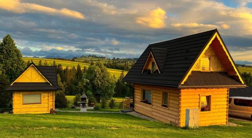 a yellow house with a black roof on a green field at Domek u Śpiewoka 1 in Maruszyna